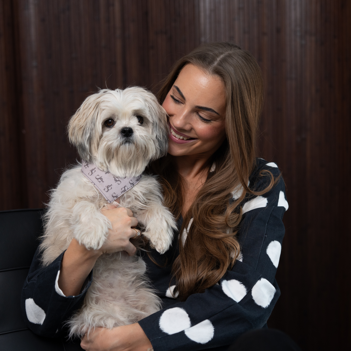 Woman in a polka-dot cardigan holding a shih tzu wearing a Staey bandana
