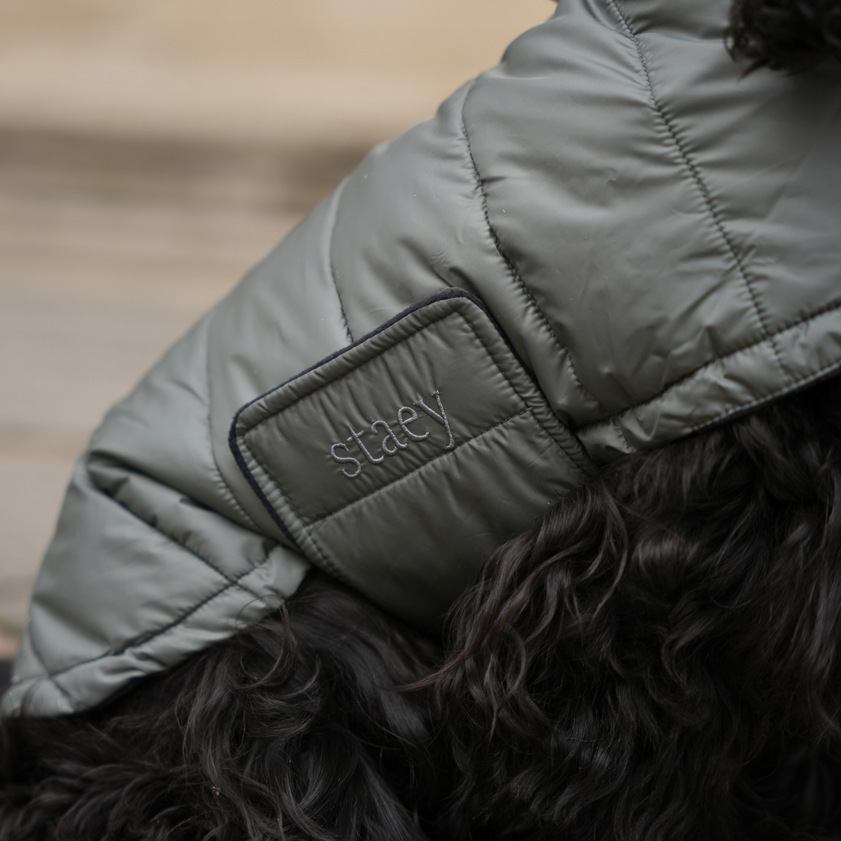 Close-up of the embossed Staey patch on the moss green quilted coat