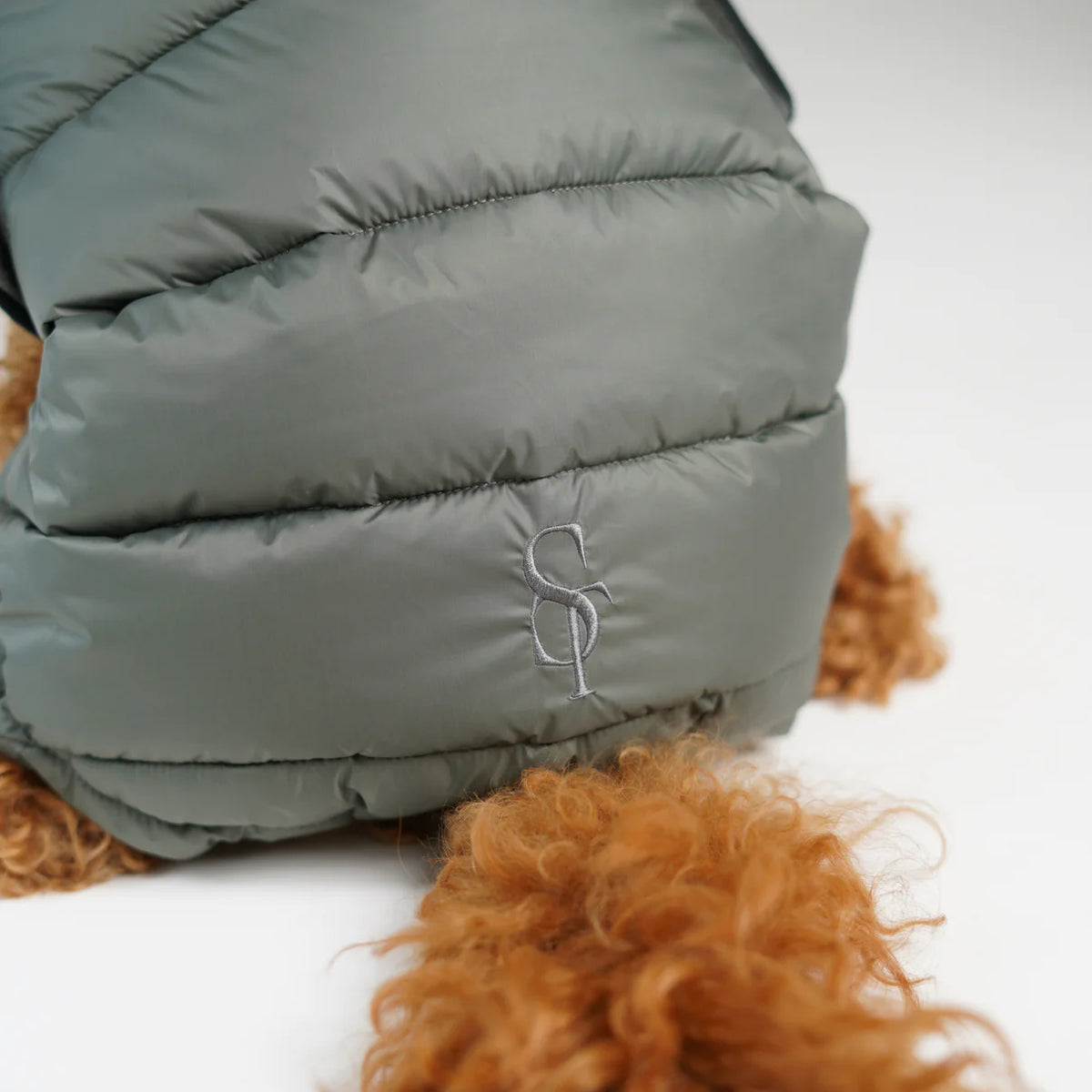 Close-up of the embossed Staey monogram on the moss green quilted coat