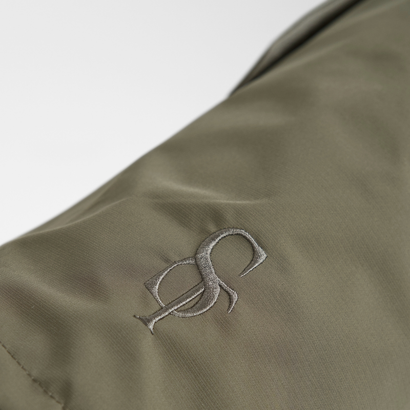 Close-up of the embossed Staey monogram on the olive green rain coat